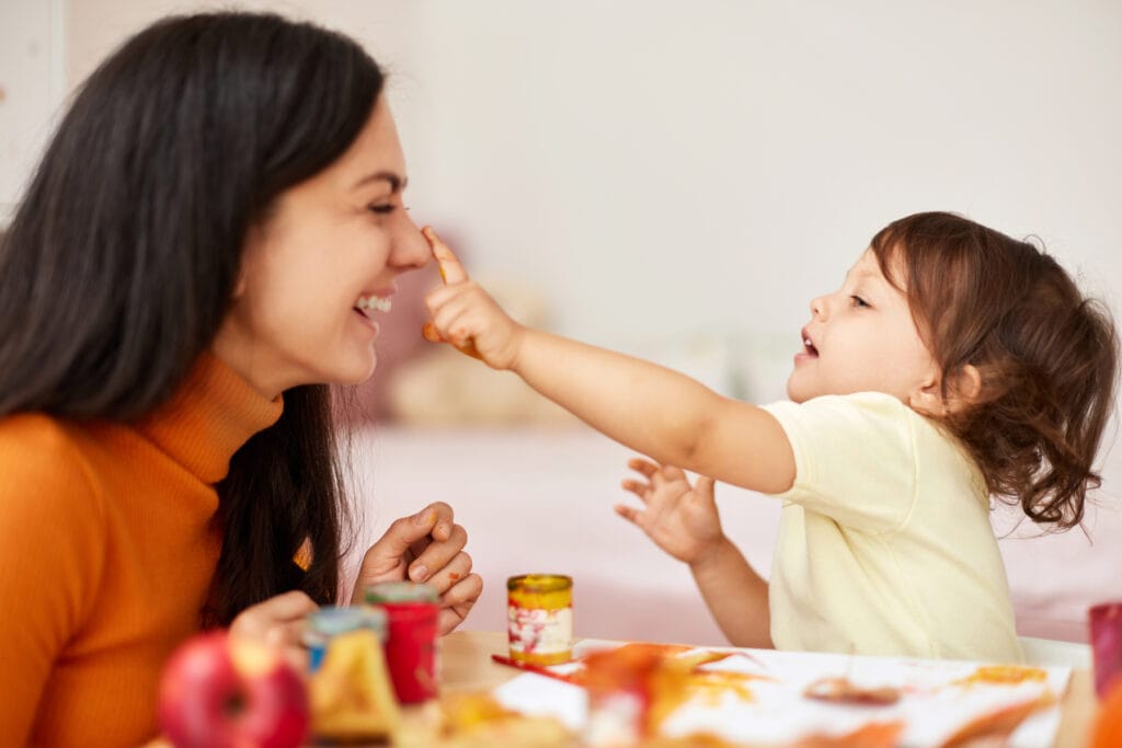 Cute little girl and mom spending good time painting autumn yellow leaves together